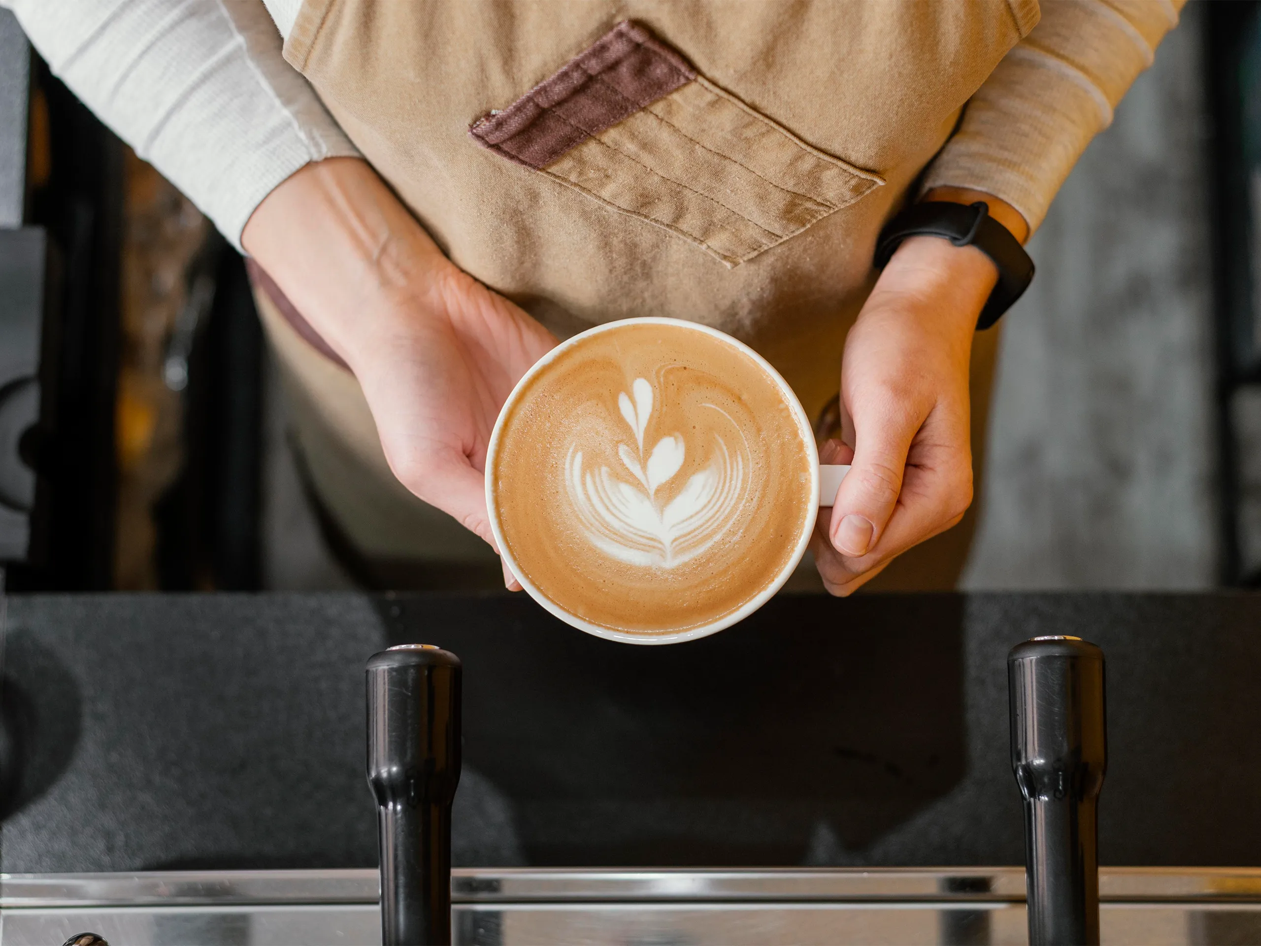 Barista überreicht eine Tasse mit frisch gezogener Latte Art