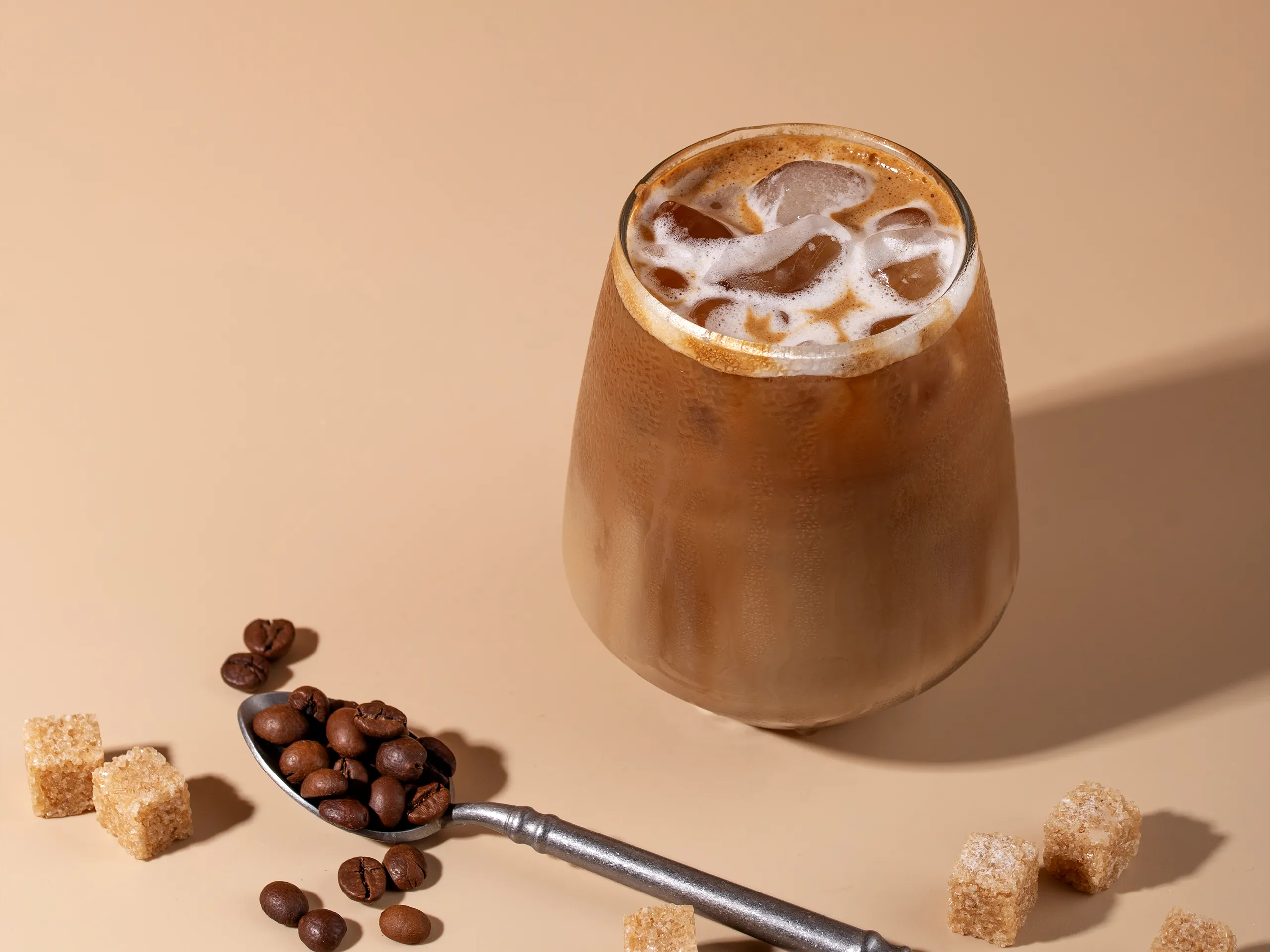 Iced Latte im Glas mit Eiswürfeln, Kaffeebohnen und braunem Zucker